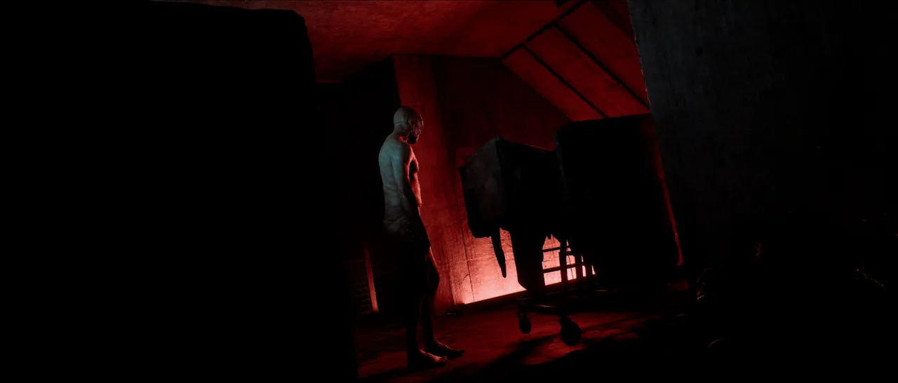 A dark room lit red, with a figure standing beside dark furniture.