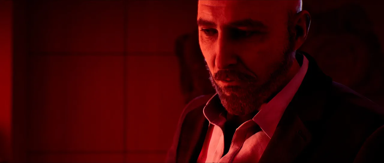A bald, bearded man lit in red, looking down.